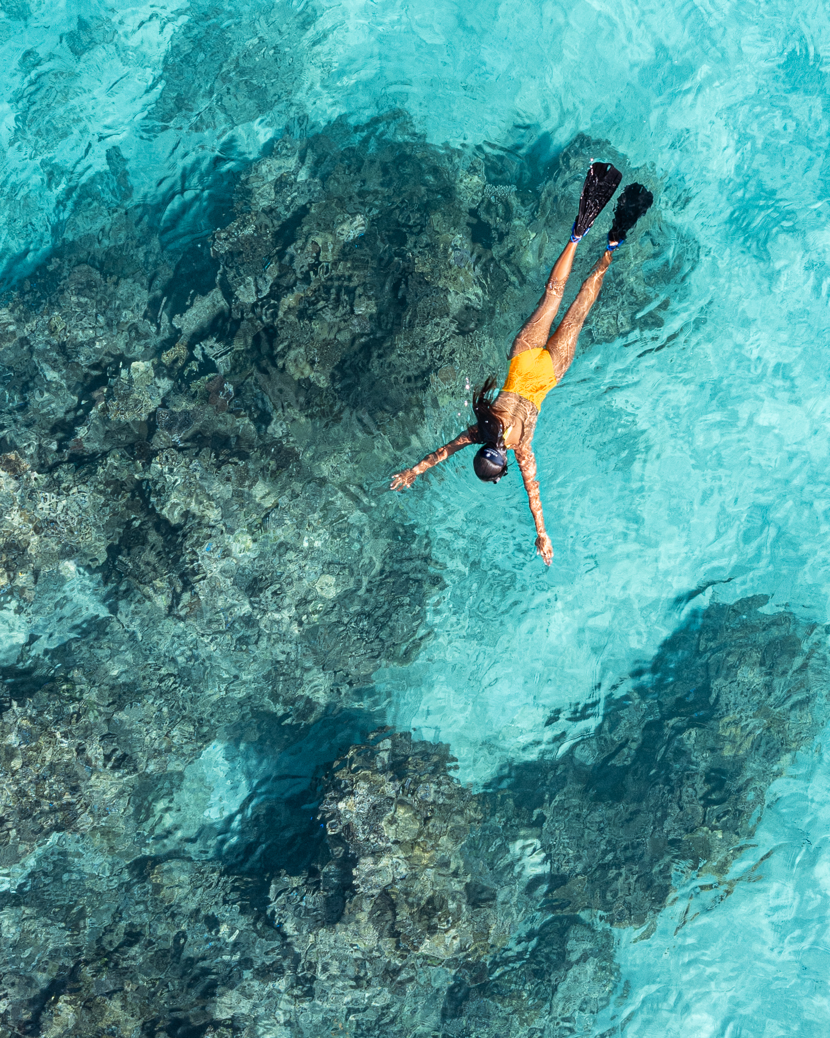 A person in a yellow swim suit floats peacefully in the clear blue ocean waters under a bright sky off the shoreline of Kokomo Private Island.