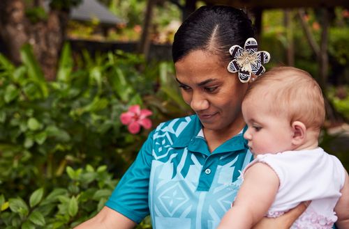 A Kokomo Private Island team member holding a child outside near a garden.