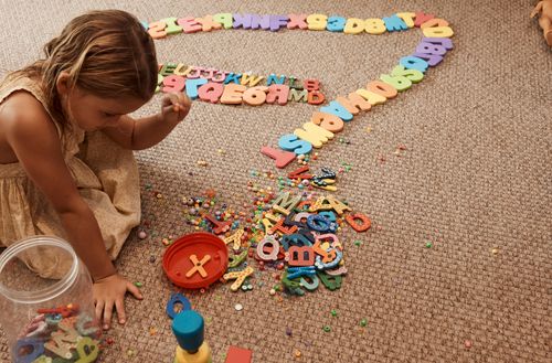 A small child playing with cut out letters and beads at Kokomo Private Island Kids Club.